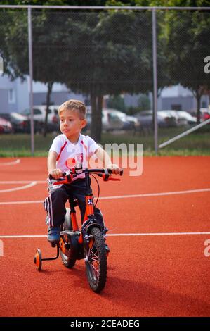 POZNAN, POLONIA - 30 agosto 2020: Giovane ragazzo caucasico polacco di tre anni seduto su una bicicletta con ruote di supporto su un campo sportivo pubblico. Foto Stock