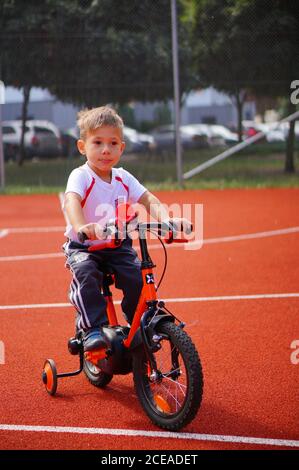 POZNAN, POLONIA - 30 agosto 2020: Giovane ragazzo caucasico polacco di tre anni seduto su una bicicletta con ruote di supporto su un campo sportivo pubblico. Foto Stock