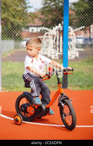 POZNAN, POLONIA - 30 agosto 2020: Giovane ragazzo caucasico polacco di tre anni seduto su una bicicletta con ruote di supporto su un campo sportivo pubblico. Foto Stock