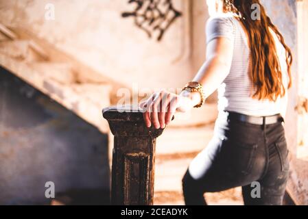 Crop giovane donna che cammina al piano superiore mentre passa il tempo in vecchio edificio abbandonato Foto Stock