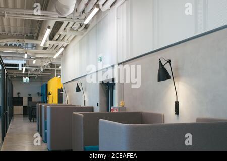 Interno grigio della caffetteria d'ufficio con tavoli e divani vuoti con alti schienali e lampade appese alle pareti Foto Stock