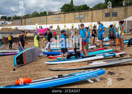 Un grande gruppo di stand up paddle boarder che si preparano a prendere le loro tavole fuori sull'estuario del Tamigi a Chalkwell Beach, Southend on Sea, Essex, Regno Unito Foto Stock
