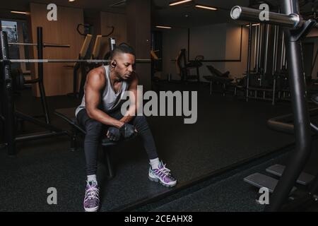 Uomo nero nelle cuffie seduto sulla macchina da ginnastica Foto Stock
