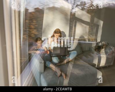 Donna e ragazza con notebook e tablet seduti sul divano Foto Stock