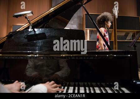 Crop uomo che suona piano mentre provando in studio di registrazione con cantante femminile. Foto Stock