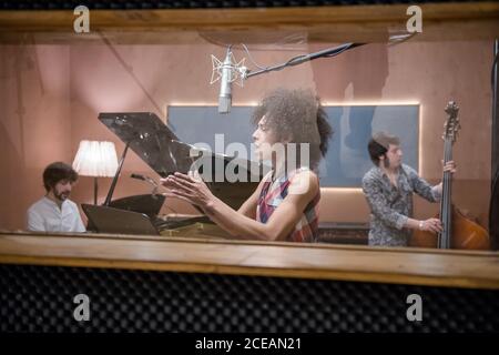 Attraente Donna cantando canzone e battendo le mani mentre prova con band in studio di registrazione. Foto Stock