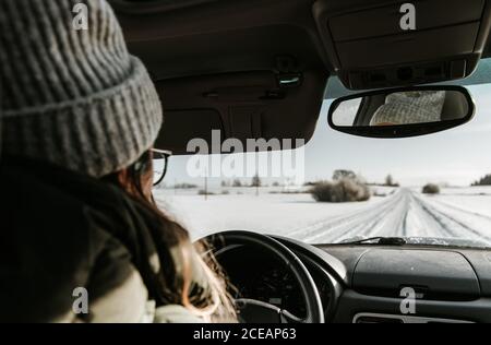 Vista posteriore di lady in hat guida automobile sulla strada di campagna nella neve tra il campo di Vilnius, Lituania Foto Stock