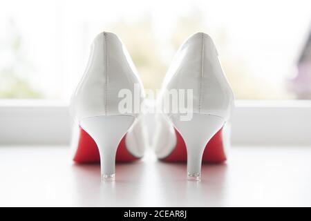 Belle scarpe classiche da sposa bianche con suola rossa posta vicino alla finestra sullo sfondo sfocato della strada Foto Stock