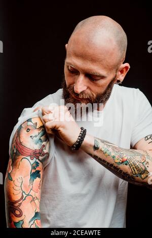 Barbuto tanga glabre in t-shirt che mostra i tatuaggi sulle mani su sfondo nero Foto Stock