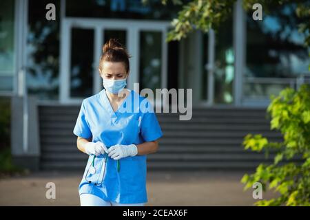 covid-19 pandemic. stanco medico moderno donna in scrub con stetoscopio e maschera medica fuori vicino clinica. Foto Stock