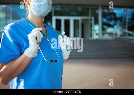 pandemia di coronavirus. Primo piano su medico donna in scrub con stetoscopio e maschera medica all'aperto vicino ospedale. Foto Stock