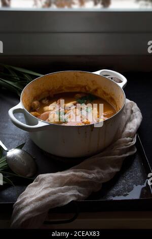 Gustosa zuppa cucinata con patate in pentola bianca servita su un tavolo. Foto Stock