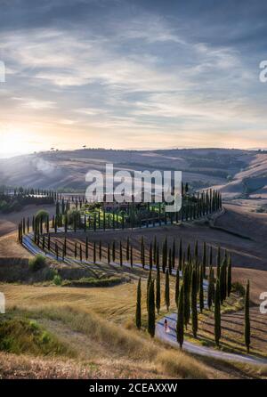 Tramonto sulla bella S curva strada in Toscana, Italia - donna in abito rosso a piedi in distanza Foto Stock