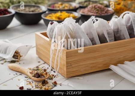 Scatola di legno di bustine di tè riempite di erbe medicinali secche e fiori. Ciotole di piante medicinali sullo sfondo. Medicina alternativa Foto Stock