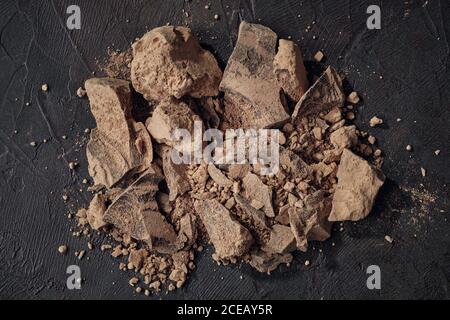 Pezzi di cacao grattugiato. Grumi di cioccolato naturale su sfondo scuro, vista dall'alto. Foto Stock