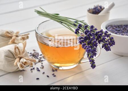 Tazza di sano tè alla lavanda e fiori alla lavanda. Mortai di lavanda secca e bustine sullo sfondo. Medicina alternativa. Foto Stock