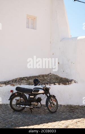 Moto nera con casco parcheggiato su†di ciottoli in alto edificio bianco con piccola finestra su sfondo blu del cielo Foto Stock