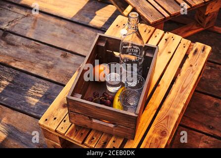 Da sopra tre bicchieri con bottiglia e uva con banana e arancio giacente in cassa di legno sulla sedia Foto Stock