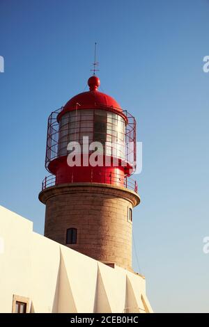 Dipinto in rosso sulla parte superiore del faro e sul fondo da mattoni su un edificio bianco sullo sfondo con cielo blu chiaro Foto Stock