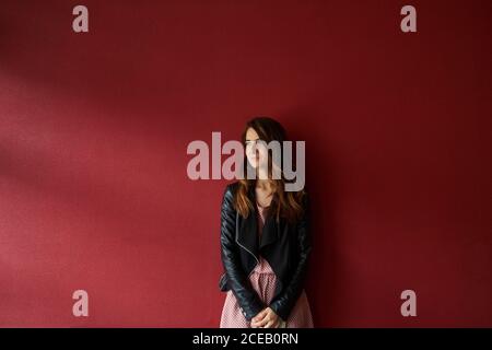 Giovane donna in giacca in piedi vicino al muro rosso Foto Stock
