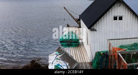 Vecchio capannone bianco di legno di pescatore con reti di granchio alla costa del mare, Norvegia Foto Stock