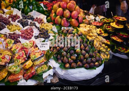 Dall'alto su molte frutta esotiche colorate e insalata con porzione di uva in confezioni di plastica con persone non riconoscibili sfondo Foto Stock