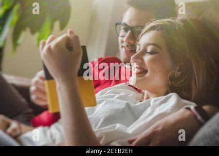 Uomo e donna allegri e sognanti sdraiati sul divano e leggendo il depliant Foto Stock