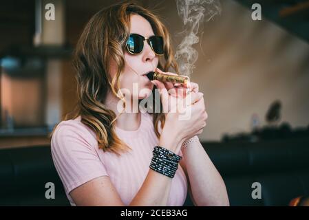 Donna che fuma marijuana in un bicchiere smussato Foto Stock