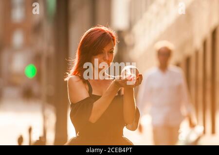 Ballerina testa rossa con tutu nero guardare attraverso un cristallo palla sulla strada con sfondo di luce posteriore al tramonto Foto Stock