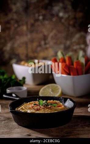 Humus di ceci fatto a casa. Con paprika, cetriolo e carota. Su vecchio tavolo di legno. Foto Stock