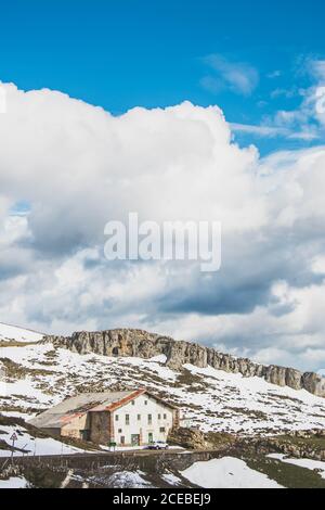 Paesaggio di casa remota con recinto di pietra sul pendio di highlands con neve primaverile sotto il cielo blu Foto Stock