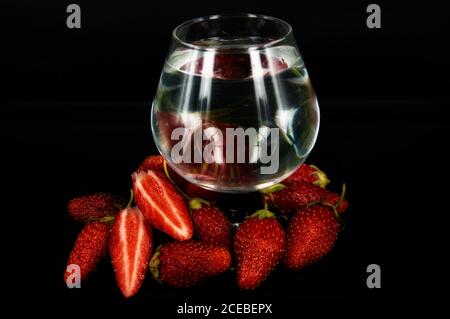 fragole intere e affettate si chiocciolano con un bicchiere d'acqua su sfondo nero Foto Stock