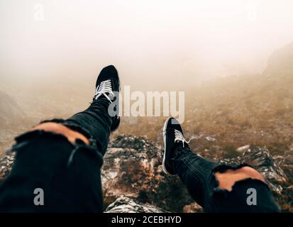 Gambe di turista irriconoscibile seduto sulla scogliera in giorno di nebbia. Foto Stock