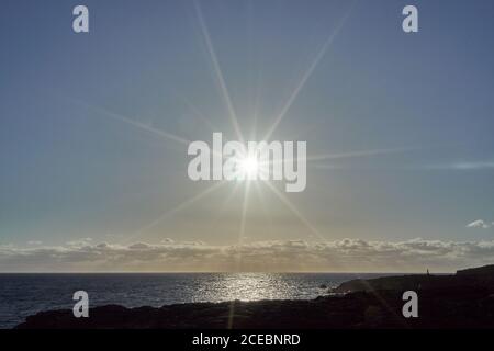 Vista di Bright sole che splende sopra il mare e la costa rocciosa Foto Stock
