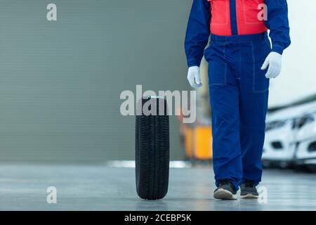 Cambio meccanico automatico pneumatico attraente meccanico uomo in blu uniforme con guanti blu che girano sulla ruota autoservice nel centesimo di riparazione automatico Foto Stock