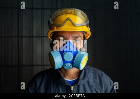 Il lavoratore asiatico indossa un respiratore in un'atmosfera tossica e affumicata. L'immagine mostra l'importanza della predisposizione alla protezione e della sicurezza nello stabilimento industriale Foto Stock