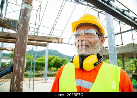 Ingegnere operaio asiatico che indossa casco e indumenti di sicurezza nel cantiere della casa. Concetto di anziano che lavora Foto Stock