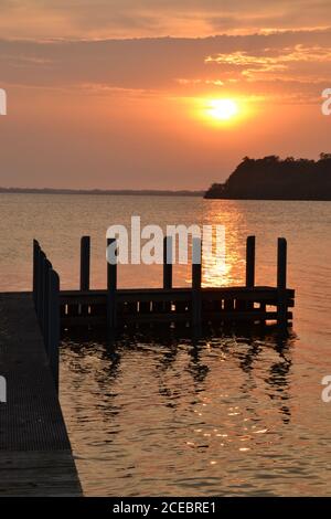 Al mattino sorge l'alba del cielo arancione a Mallacoota, con un molo e un promontorio in silhouette Foto Stock