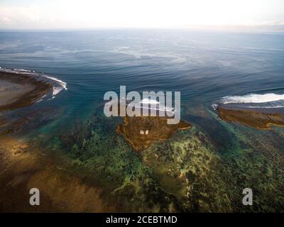 Vista aerea della vasta superficie dell'acqua di mare con pittoresca poco profonda baia e piccola isola con edifici su di esso al sole giorno Foto Stock