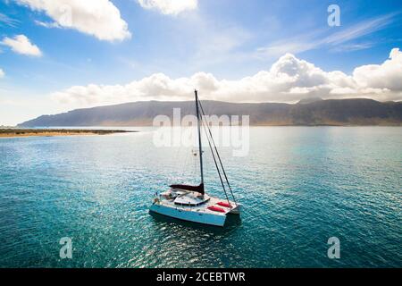 Vista aerea di un piccolo yacht che naviga nella pittoresca baia sulla costa rocciosa dell'oceano durante la soleggiata giornata estiva a la Graciosa, Isole Canarie Foto Stock