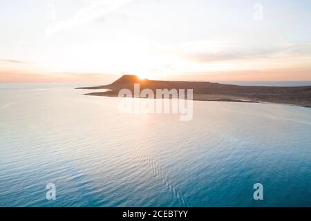 Pittoresca vista aerea della bellissima costa rocciosa della penisola circondata da calmo mare blu con tramonto dietro la cima della scogliera a la Graciosa, Isole Canarie Foto Stock