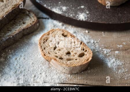 Fette di pane fresco appetitoso messo in farina su ruvido tavolo di legno Foto Stock