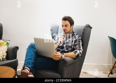 Giovane uomo che usa il computer portatile sulla poltrona Foto Stock