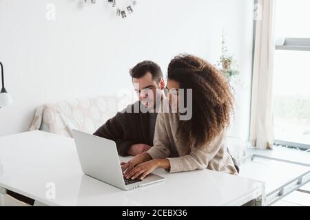 Allegra coppia multietnica che usa il computer portatile insieme Foto Stock