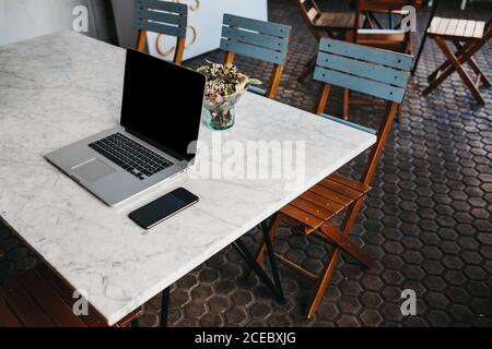 Tavolo con computer portatile e smartphone sulla parte superiore con piccolo vaso di fiori in caffetteria Foto Stock