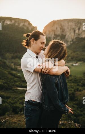 Simpatica coppia agguantata e tenace fronte mentre in piedi su sfondo di bella valle e montagne Foto Stock