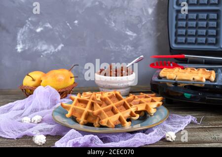 Gustosi waffle viennesi croccanti su un piatto, waffle ferro da stiro sullo sfondo. Processo di cottura dei wafer. Foto Stock