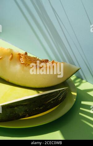 Metà pelle di melone tagliata a fetta. Tema estivo colorato. Su sfondo blu e verde, ombre di foglie di palma Foto Stock