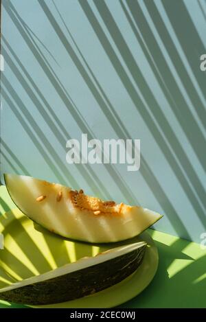 Metà pelle di melone tagliata a fetta. Tema estivo colorato. Su sfondo blu e verde, ombre di foglie di palma Foto Stock