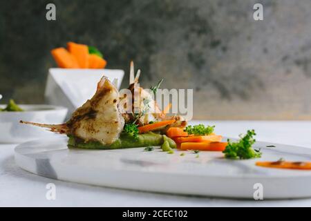 pesce scorpione alla griglia con purè di piselli e bastoncini di carote, su un piatto di marmo Foto Stock